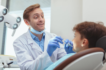 Professional dentist talking to his little patient joyfully, while examining his teeth, copy space....
