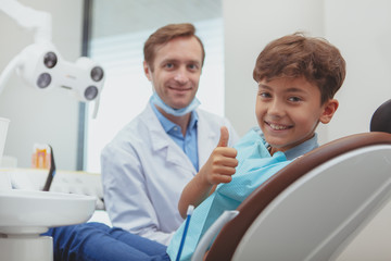 Happy healthy kids concept. Charming young boy smiling, showing thumbs up after dental examination at the clinic. Happy boy smiling with healthy teeth after visiting dentist