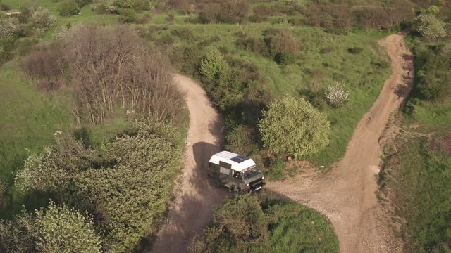 Aerial view vehicle moving on sandy road. Tourist car passes through rural fields on mountain landscape. Travel by van car. Summer cat trip. Tourism by vehicle