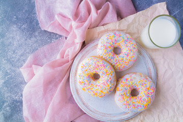 American sweetness glazed donuts and a glass of milk on a gray surface against a background of pink cloth close-up above the head top view