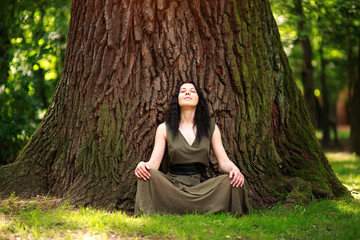 Girl in dress sits enjoying nature meditates, practices yoga in forest