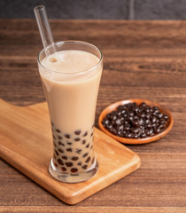 Popular Taiwan drink - Bubble milk tea with tapioca pearl ball in drinking glass and straw, wooden table gray brick background, close up, copy space