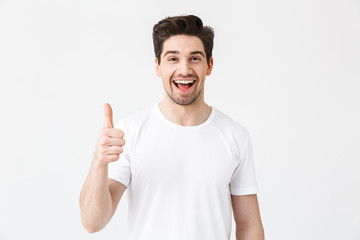 Excited young man posing isolated over white wall background showing thumbs up gesture.