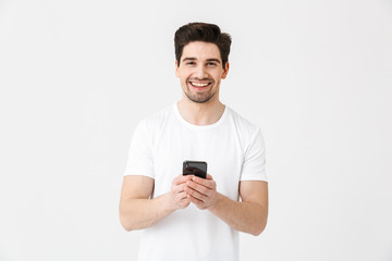 Excited happy young man posing isolated over white wall background using mobile phone.