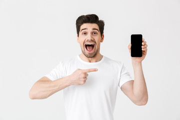 Excited happy young man posing isolated over white wall background showing display of mobile phone.