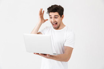 Shocked excited young man posing isolated over white wall using laptop computer.