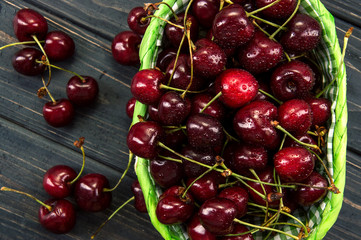 Top view, flat lay. Close up. Ripe maroon cherries in a green wicker basket.
