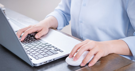 Business concept. Woman in blue shirt typing on computer with coffee on office table, backlighting, sun glare effect, close up, side view, copy space