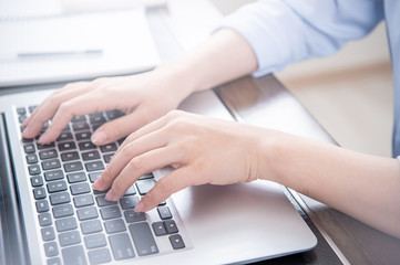 Business concept. Woman in blue shirt typing on computer with coffee on office table, backlighting, sun glare effect, close up, side view, copy space