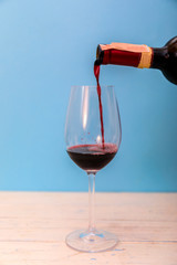 Pouring red wine into the glass against wooden background.