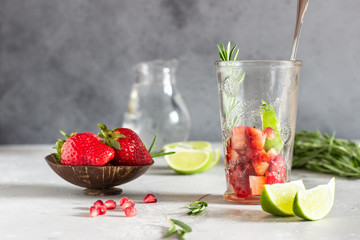 Strawberry lemonade and ingredients (strawberry, pomegranate, rosemary and lime) on light grey background. Copy space.