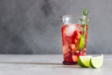 Homemade strawberry lemonade in glass with fresh strawberries, rosemary, pomegranate and lime over light grey stone table. Refreshing summer drink. Cocktail bar background concept. Copy space.