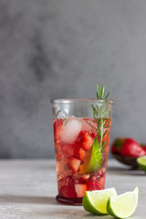 Homemade strawberry lemonade in glass with fresh strawberries, rosemary, pomegranate and lime over light grey stone table. Refreshing summer drink. Cocktail bar background concept. Copy space.