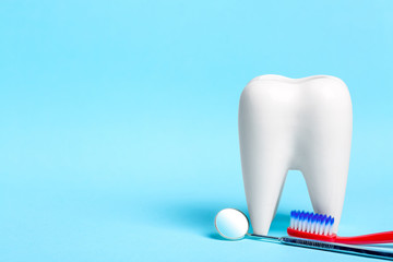 Fototapeta na wymiar Oral dental hygiene. Dental mirror with toothbrush near healthy white tooth model on light blue background. Free space for your text.