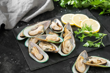 Raw kiwi mussels in a black plate on a dark background