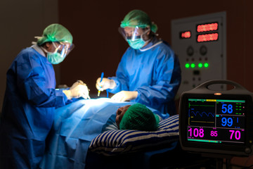 Electrocardiogram in hospital surgery operating emergency room showing patient heart rate with blur team of surgeons in background. Health and medicine concept..