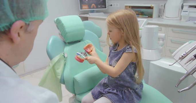 Smiling little girl in dentists chair being educated about proper tooth-brushing by her pediatric dentist