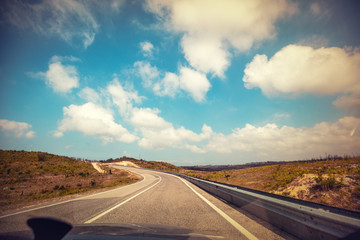 Driving a car on a winding mountain road in Portugal on a sunny day with a cloudy sky