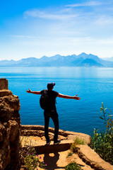 Fototapeta na wymiar Young man stands on a rock on the background of a beautiful view of the Mediterranean Sea and mountains. Turkey, Antalya.