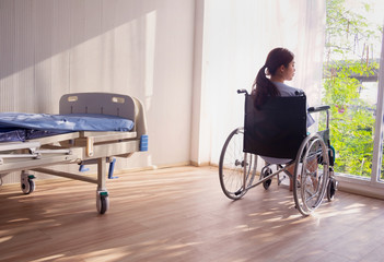 The woman sitting on wheelchair. She is see window with patient bed in hospital. disabled person,...