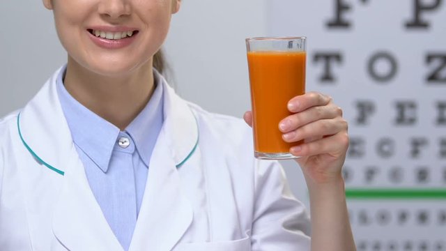 Smiling female doctor showing carrot juice against eye chart background, health