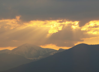 Morning landscape with mountains and orange sky at sunrise with sun reflecting. Evening sunset on the horizon of hills with snow and sun rays.