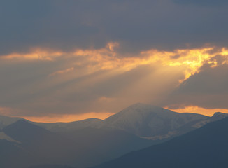 Morning landscape with mountains and orange sky at sunrise with sun reflecting. Evening sunset on the horizon of hills with snow and sun rays.