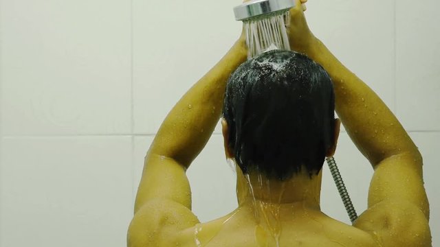 The Back Of Asian Men Wet Water From The Shower In Hand  Within The Bathroom.