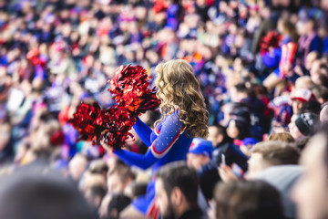 Female cheerleader in red blue uniform with pom-pom with audience in the background performing and...