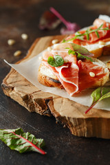 Traditional parma cured ham antipasto. Bruschetta set with Parma Ham and Parmesan Cheese. Small sandwiches with prosciutto, parmesan cheese, fresh arugula, olives and pine nuts