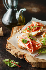 Traditional parma cured ham antipasto. Bruschetta set with Parma Ham and Parmesan Cheese. Small sandwiches with prosciutto, parmesan cheese, fresh arugula, olives and pine nuts