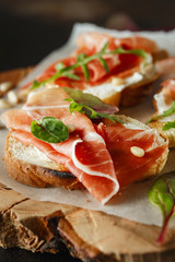 Traditional parma cured ham antipasto. Bruschetta set with Parma Ham and Parmesan Cheese. Small sandwiches with prosciutto, parmesan cheese, fresh arugula, olives and pine nuts