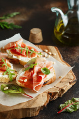 Traditional parma cured ham antipasto. Bruschetta set with Parma Ham and Parmesan Cheese. Small sandwiches with prosciutto, parmesan cheese, fresh arugula, olives and pine nuts