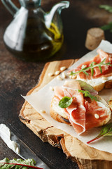 Traditional parma cured ham antipasto. Bruschetta set with Parma Ham and Parmesan Cheese. Small sandwiches with prosciutto, parmesan cheese, fresh arugula, olives and pine nuts