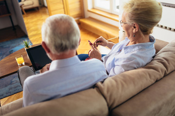 Senior woman knitting woollen clothes and her husband is using digital tablet.