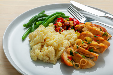 Homemade tasty chicken fillet with green beans, mashed potato and vegetable sauce on a round white plate. Traditional healthy meal. Close-up shot.
