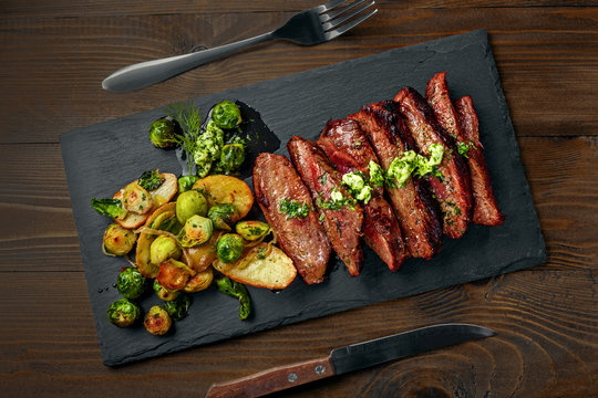 Medium rare meat hanger steak with brussels sprouts, potatoes and onion with herb sauce on a table.. Delicious healthy food. Top view above.