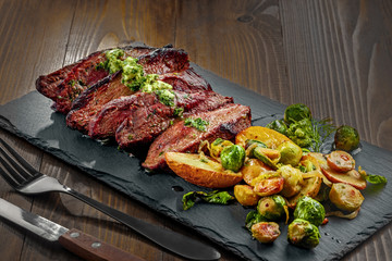 Delicious pan-seared steak with vegetables on a stone board. Meat meal with brussels sprouts, potatoes, onions and herb butter.