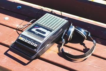 Retro vintage old 80s , 90s style portable radio audio cassette recorder player with audio tape cassette inside  with retro headphones on bench