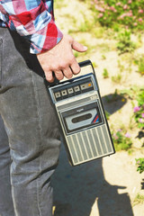 Hipster fancy man in plaid shirt holding in hand and walking with retro vintage old 80s , 90s style portable radio audio cassette recorder player boombox with audio tape cassette inside 