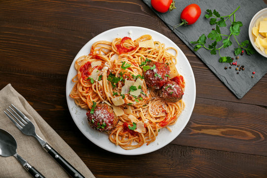 Delicious spaghetti pasta with meatballs and tomato sauce on a plate. Traditional American Italian food on a rustic wooden table. Top view shot directly above.