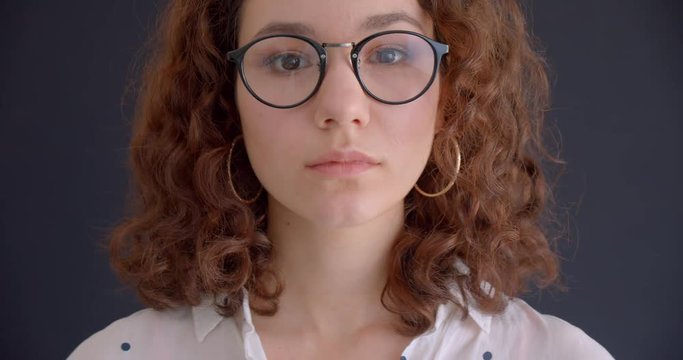 Closeup portrait of young pretty long haired curly caucasian female in glasses looking at camera with background isolated on gray