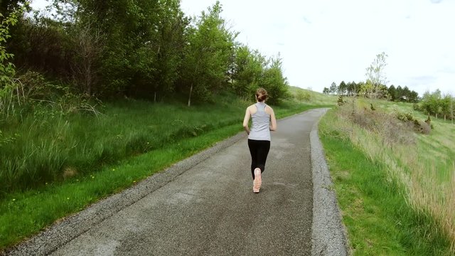Young woman running up a grass covered hill. Slow Motion