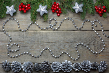 Christmas card concept with fir tree branches, rowan berries, silver cones, bead chain and silver glitter stars on wooden background - text space