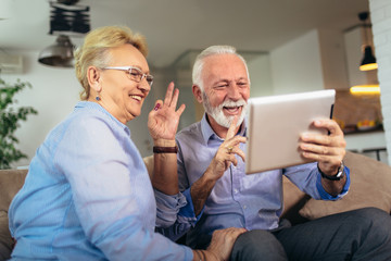 Smiling deaf senior couple talking using sign language on the digital tablet's cam