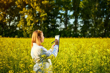 Agronomist woman or farmer examine blossoming rape (canola) field using tablet