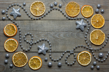 Christmas composition with silver bead chain, brocade stars and balls, and orange slices on wooden background