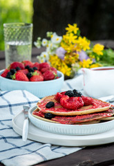Delicious summer breakfast outdoors. Pancakes with strawberries, mulberry and strawberry sauce on the garden table, rustic style.