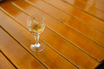A glass of cognac is standing on a wooden table on a summer evening. Strong drinks. Close up.