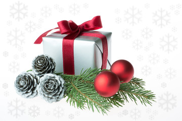 Christmas composition with a gift wrapped with red ribbon, silver cones, red baubles and a fir tree branch - isolated on white background with snow flakes